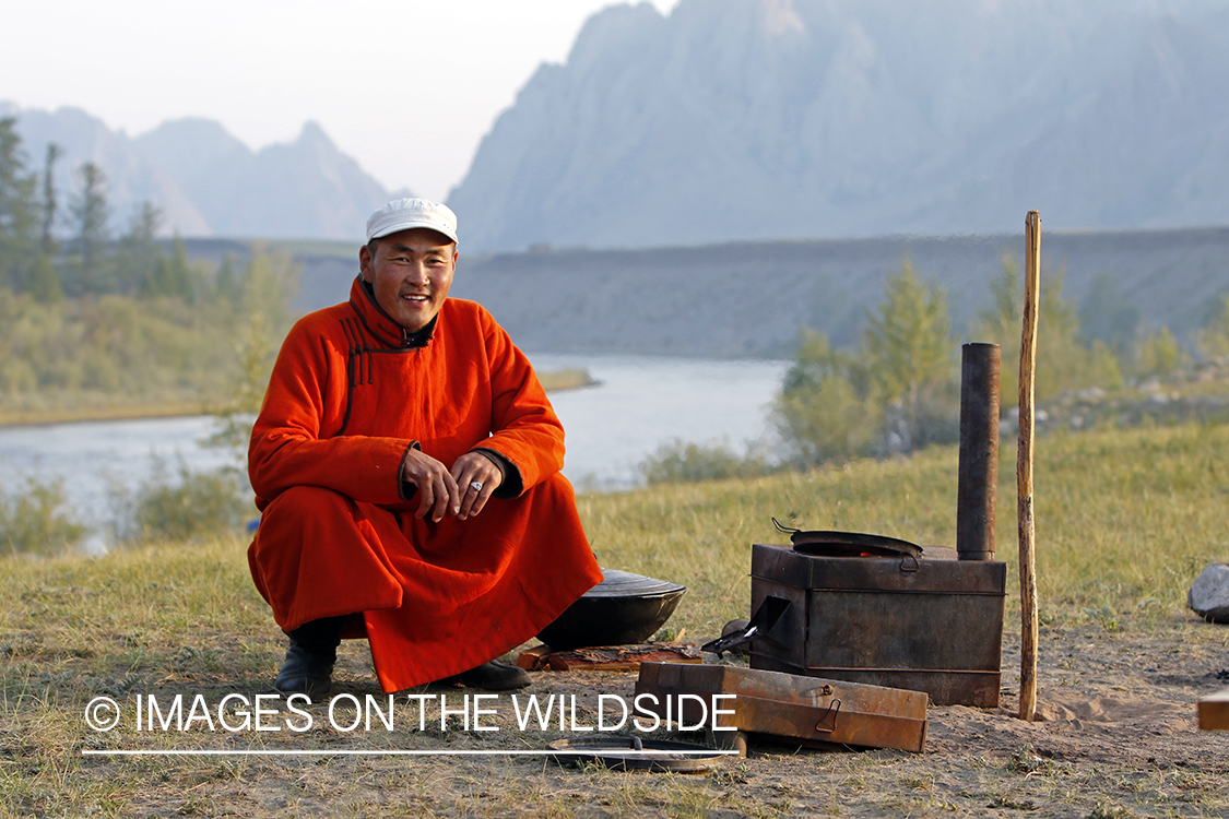 Mongolian man in native dress next to campfire.