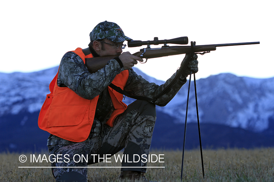 Big game hunter taking aim in field. 