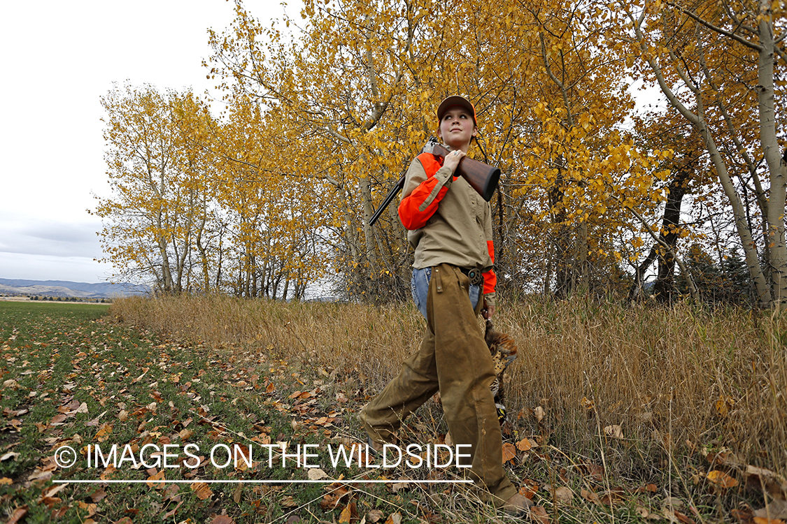 Woman with bagged pheasant walking field line.