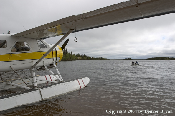 Fisherman setting off in a fishing boat with float plane tied up at the dock.  Saskatchewan.