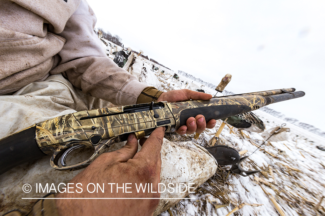 Hunter loading gun in field with decoys.