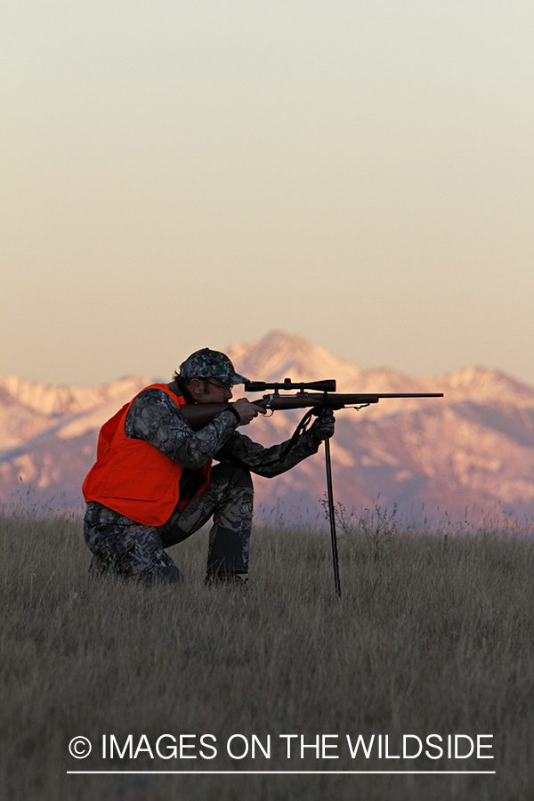 Big game hunter taking aim in field. 