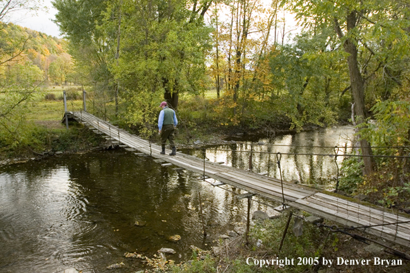 Flyfisherman crossing foot bridge over Pennsylvania spring creek.