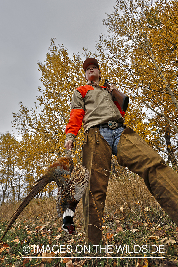 Woman with bagged pheasant walking field line.