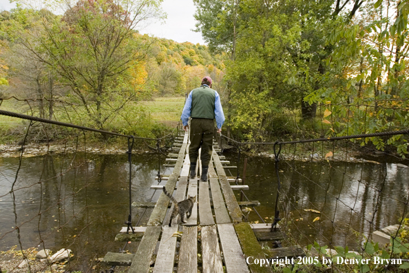 Flyfisherman crossing creek on foot bridge.