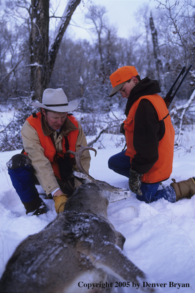 Father and son hunters with whitetail deer in a field in winter.