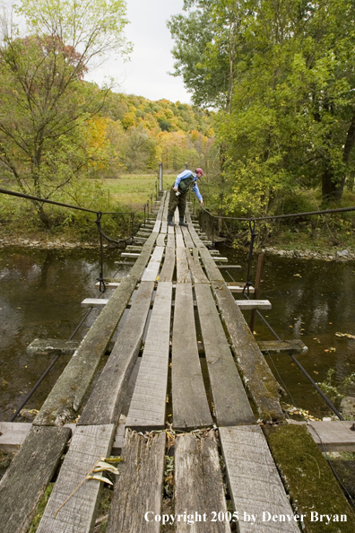 Flyfisherman crossing creek on foot bridge.