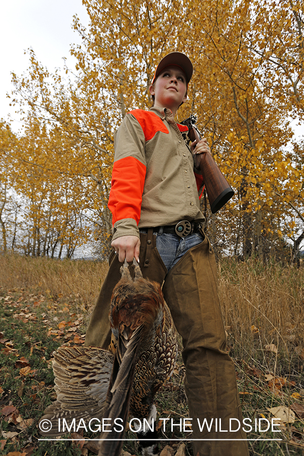 Woman with bagged pheasant walking field line.