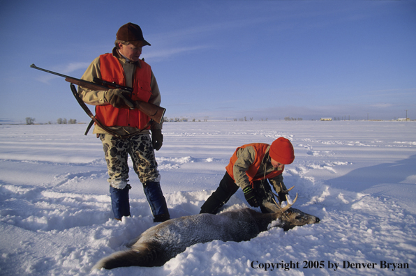 Father and son hunters with bagged whitetail deer in a snow covered field in winter.