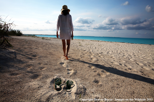 Woman walking beach to go flyfishing.                                