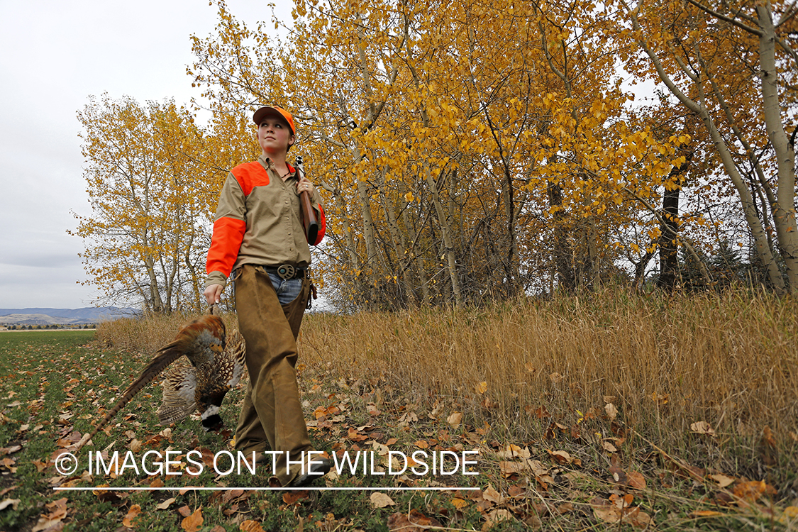 Woman with bagged pheasant walking field line.