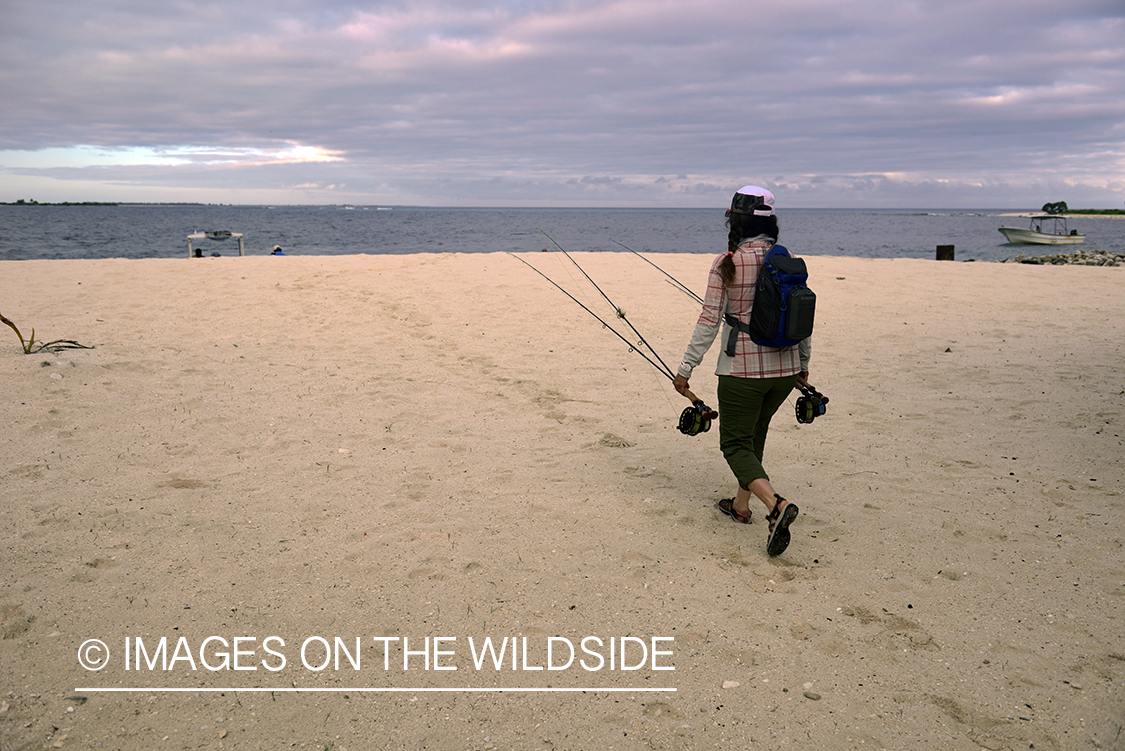 Woman walking on beach with fly rods.