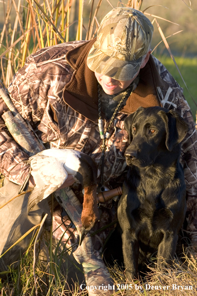 Duck hunter and Labrador Retriever at edge of marsh with bagged canvasback drake.