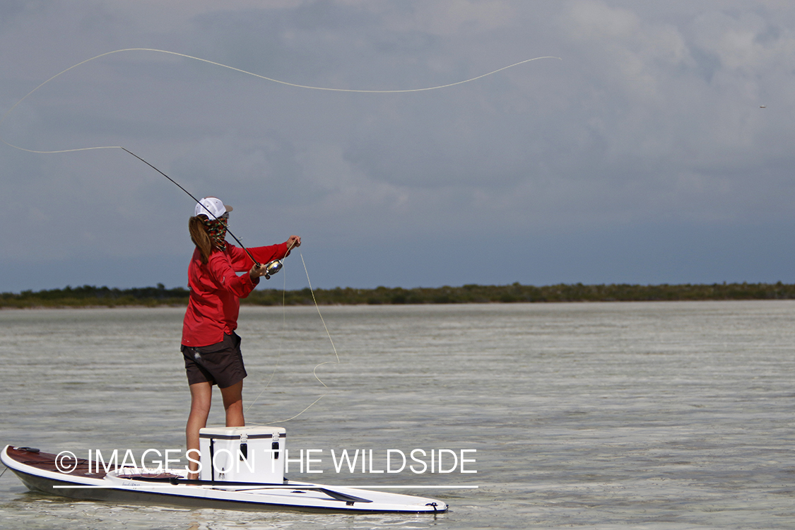 Saltwater flyfishing woman on stand up paddle board casting line.
