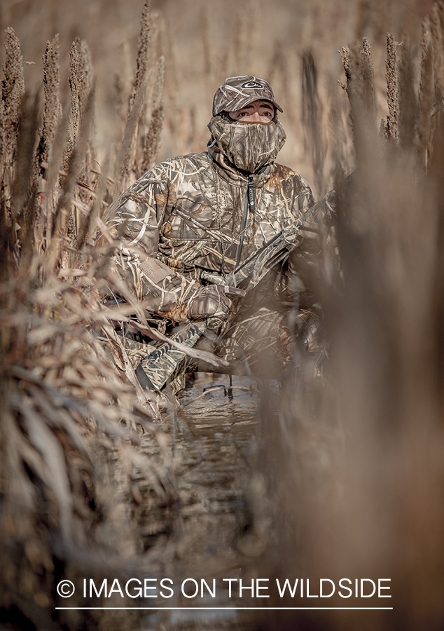 Waterfowl hunter camouflaged in wetlands.