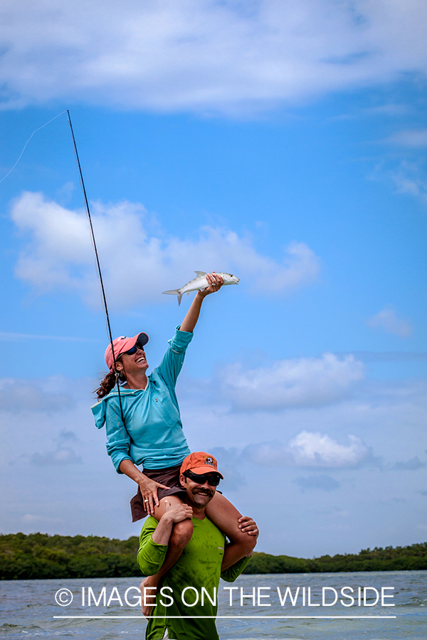 Woman flyfisher with bonefish on guides shoulders.