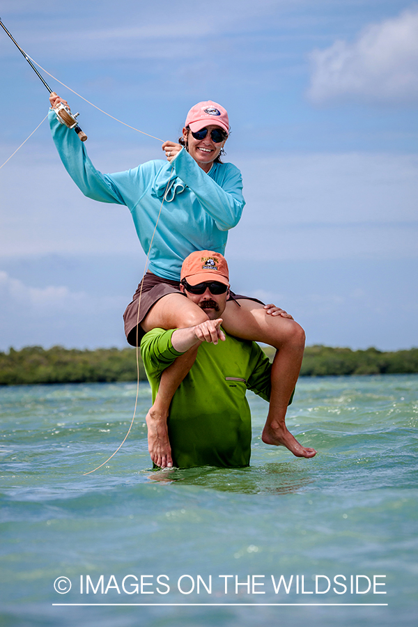 Woman flyfisher with bonefish on guides shoulders.