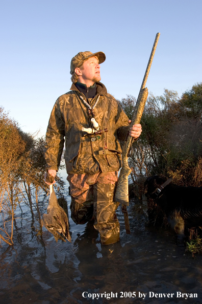 Waterfowl hunter at edge of marsh with bagged bird.