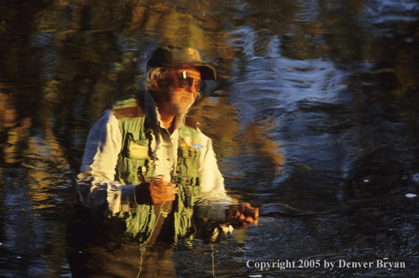 Reflection of flyfisherman on autumn colored stream.