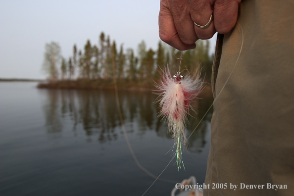 Flyfisherman holding fly, looking out from boat.