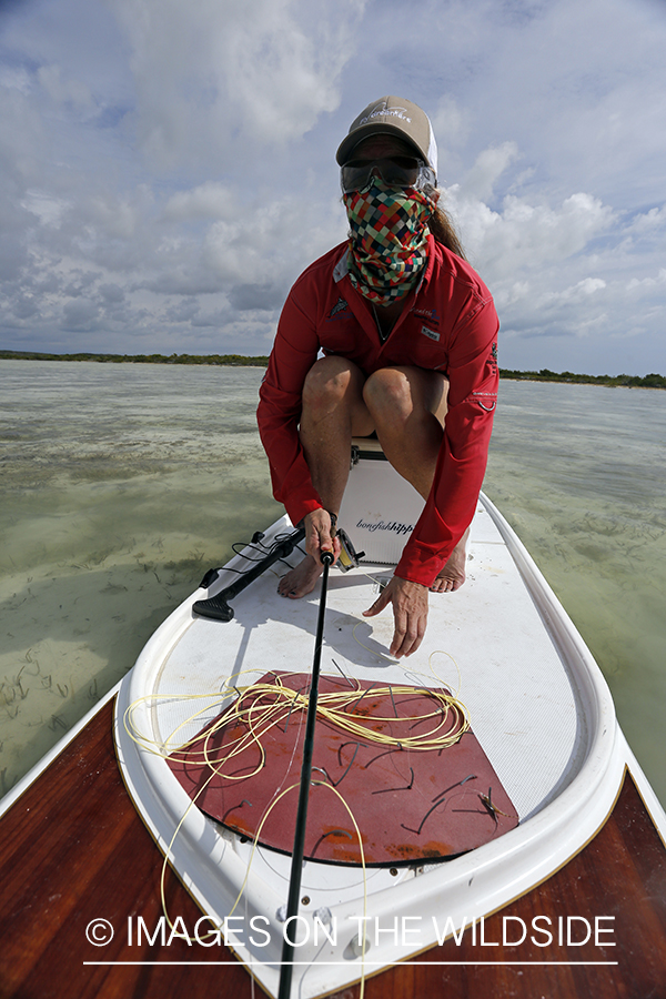 Saltwater flyfishing woman on paddle board with fishing rod.