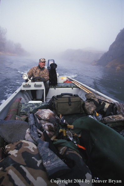 Waterfowl hunter with black Lab on boat.