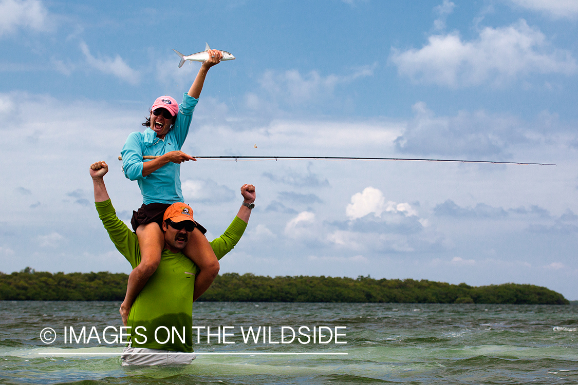 Flyfishing woman on man's shoulders with bonefish.