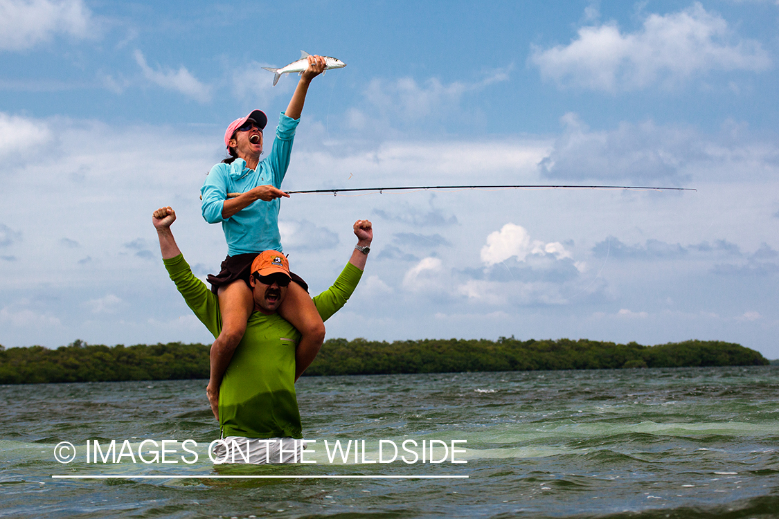 Flyfishing woman on man's shoulders with bonefish.