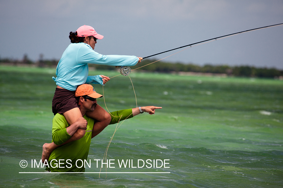 Flyfishing woman on man's shoulders casting line.