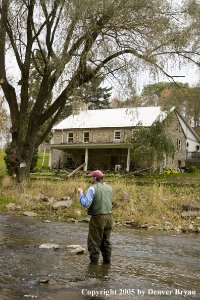 Flyfisherman on Pennsylvania spring creek with fishing club in background.