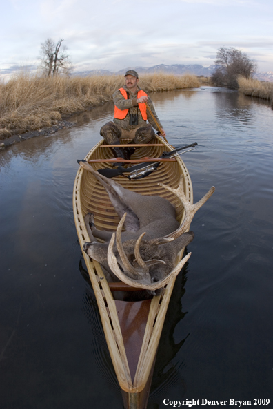 Big game hunter paddling canoe with bagged white-tail deer in bow