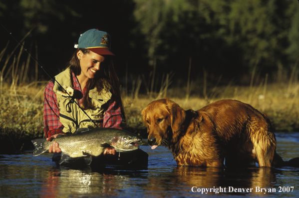 Woman flyfisher with catch and yellow Lab.