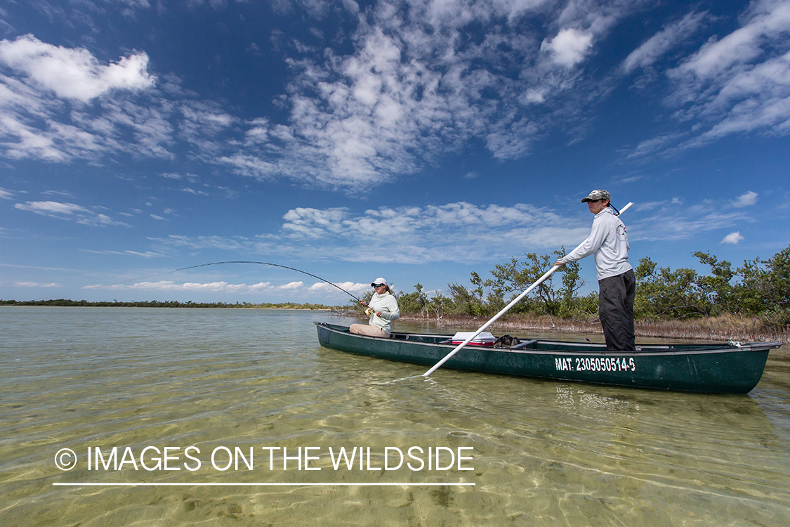 Flyfishing woman fighting fish from boat.