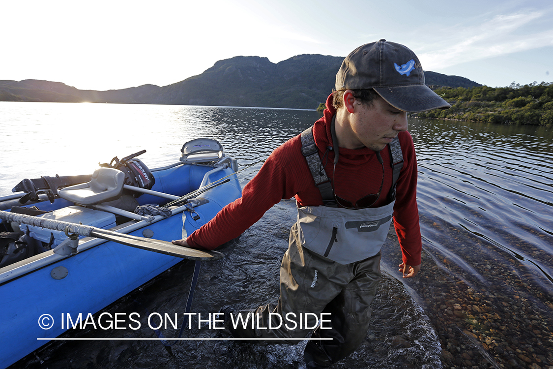 Flyfisherman dragging raft across lake shallows.