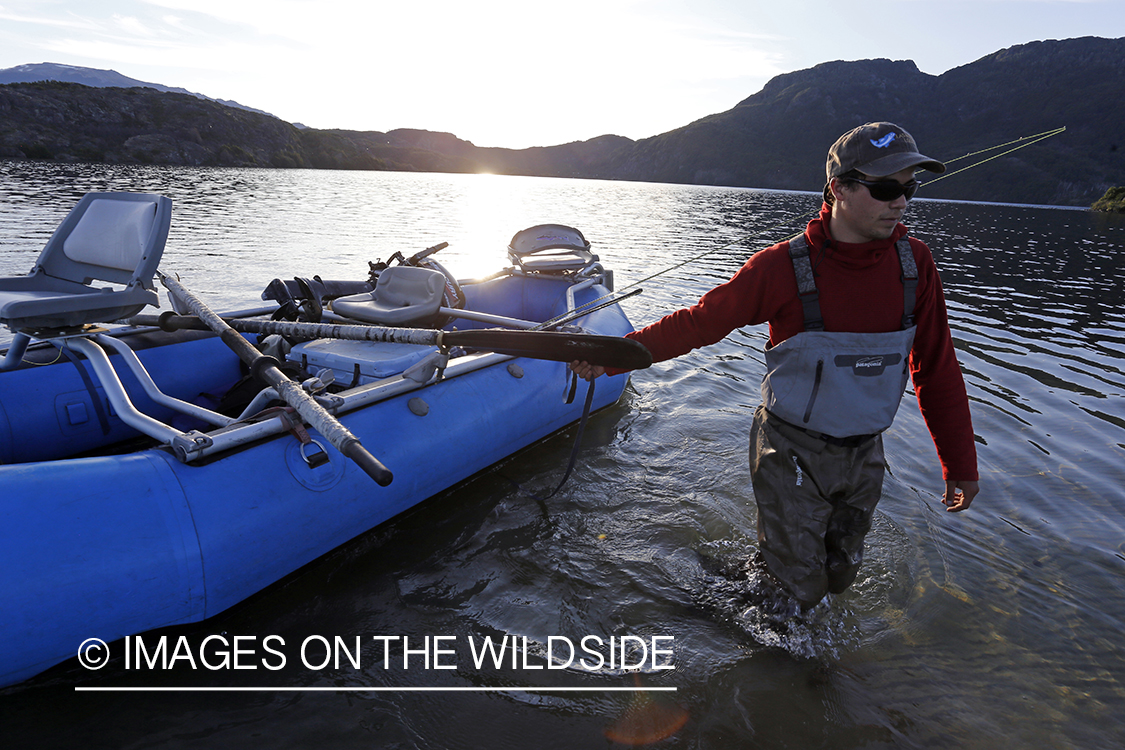 Flyfisherman dragging raft across lake shallows.