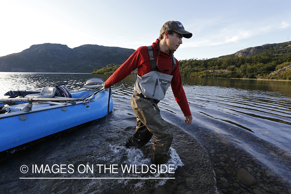 Flyfisherman dragging raft across lake shallows.