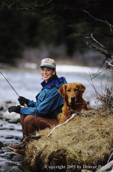 Female flyfisher sitting on river bank.