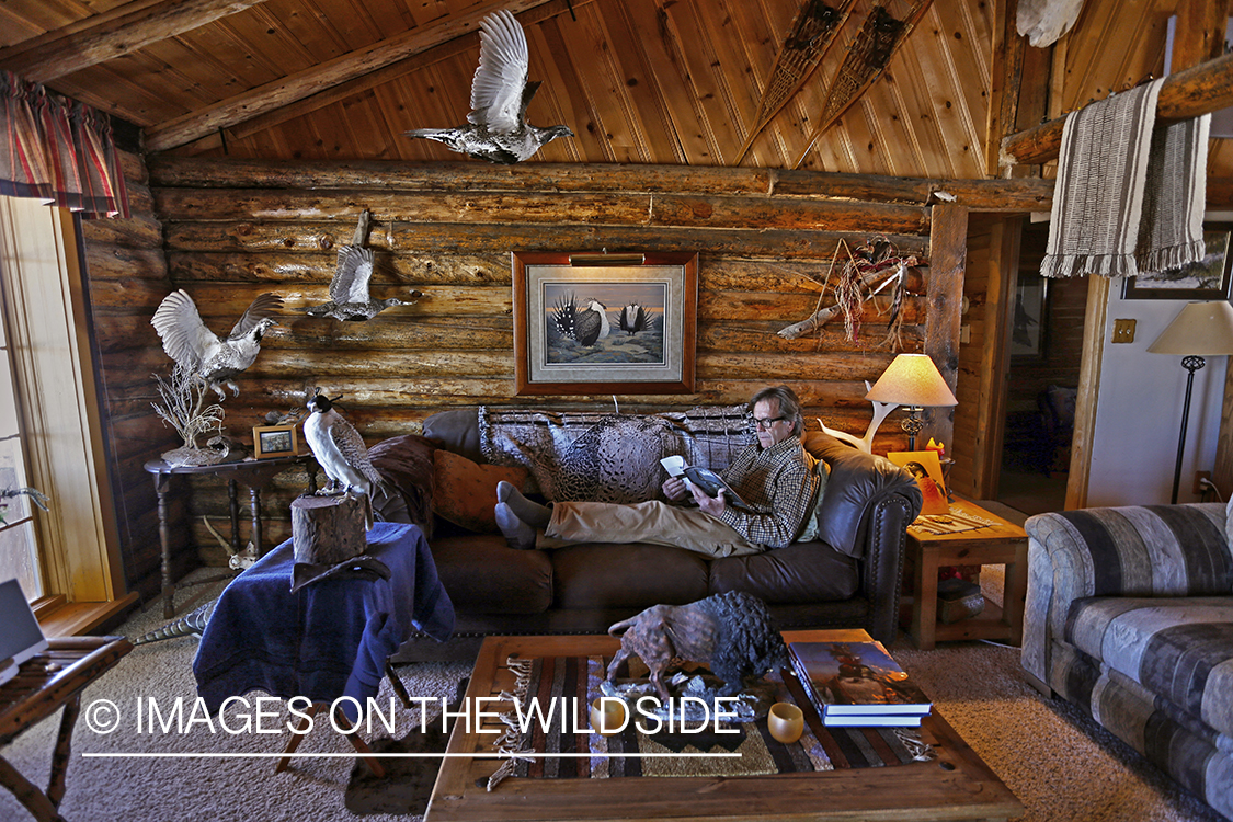 Falconer lounging in cabin with hooded gyr falcon.