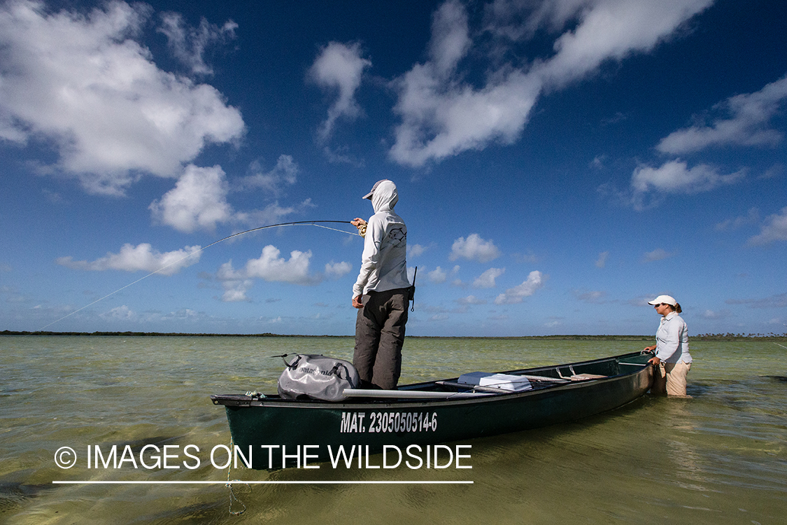 Flyfishing woman fighting fish from boat.