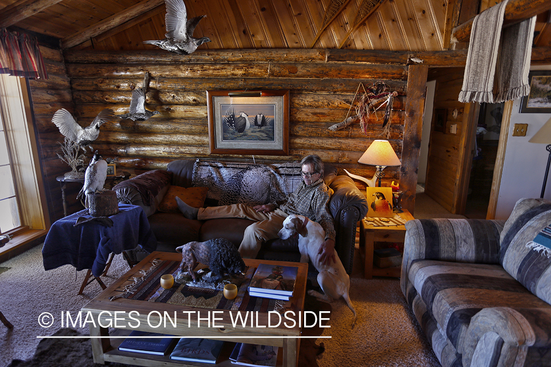 Falconer lounging in cabin with hooded gyr falcon.