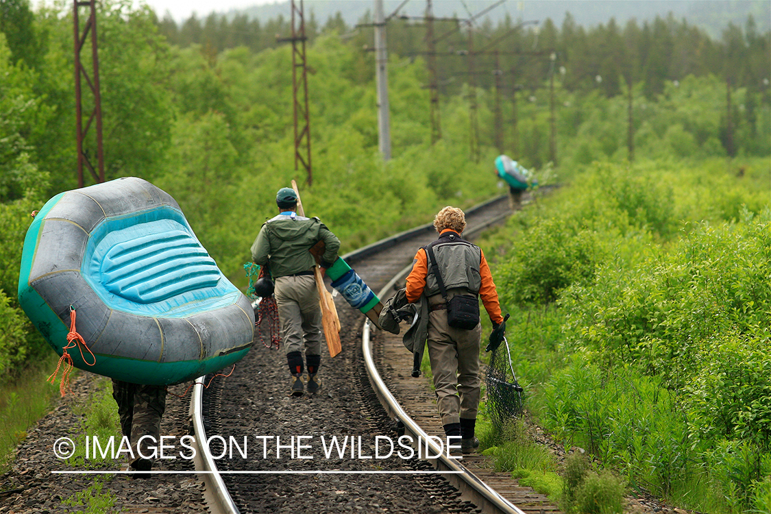 Flyfishermen packing gear down railroad tracks.