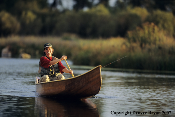 Woman flyfisher in cedar canoe.