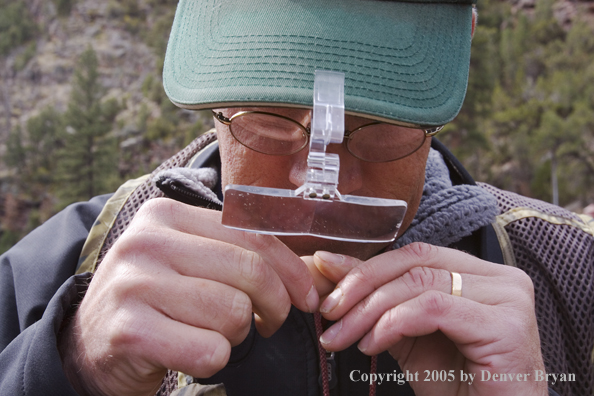 Flyfisherman using magnifying glasses to tie on fly.