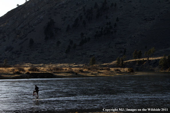 Flyfisherman tying fly on line from ladder in middle of river.