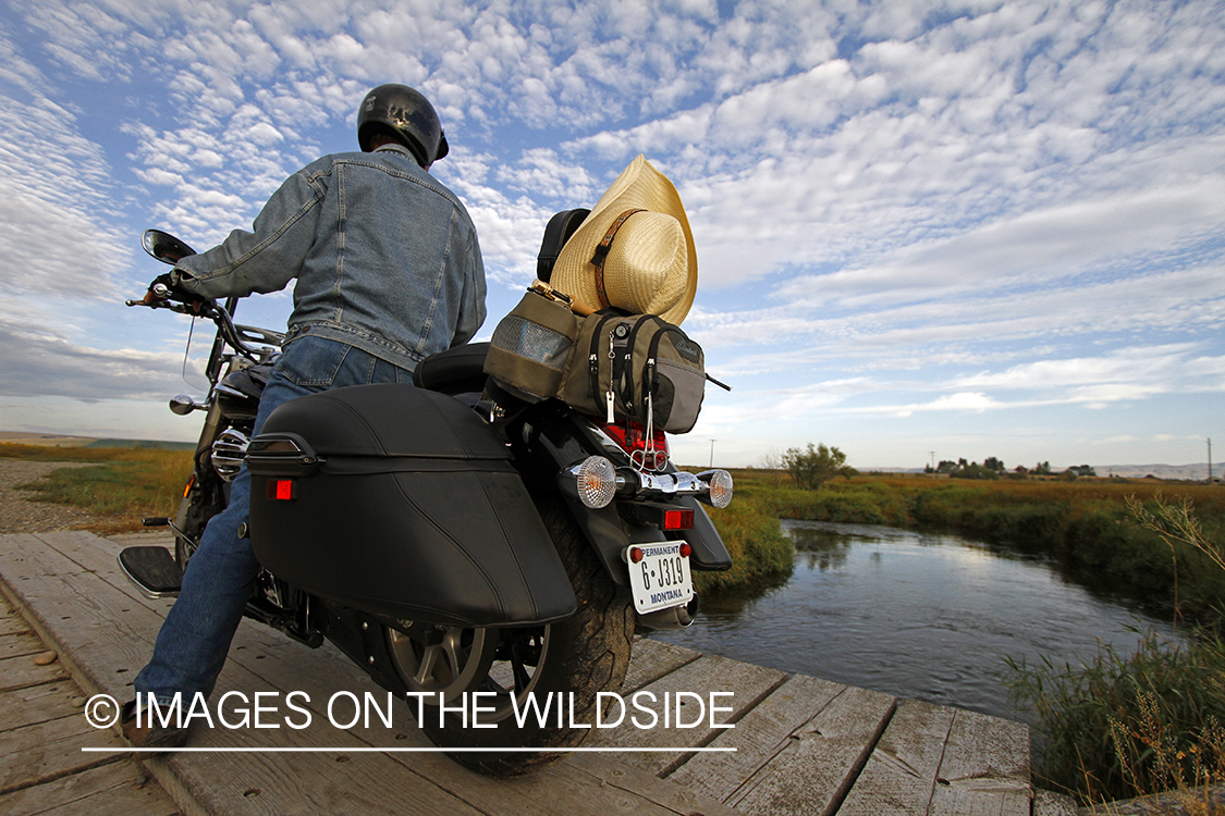 Flyfisherman on motorcyle checking stream for fish.