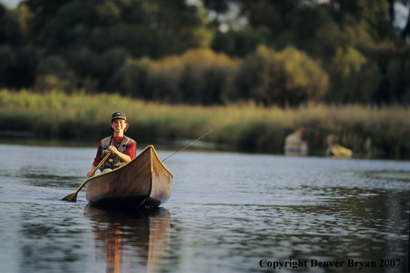 Woman flyfisher in cedar canoe.