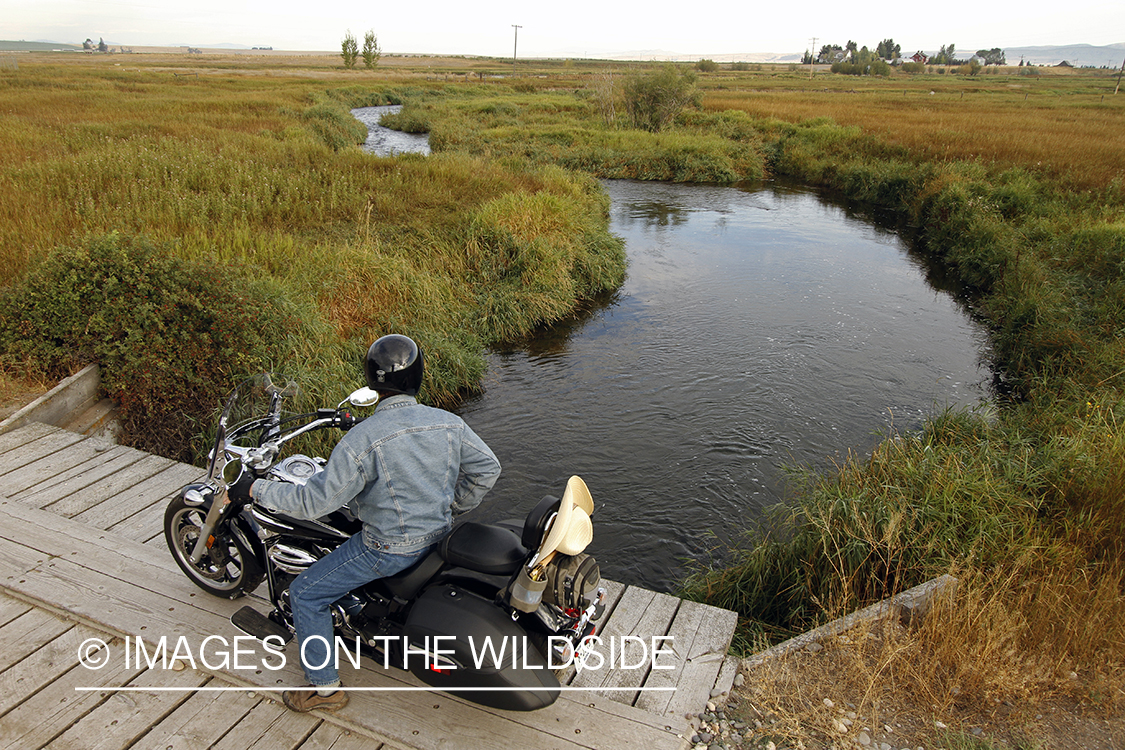 Flyfisherman on motorcyle checking stream for fish.