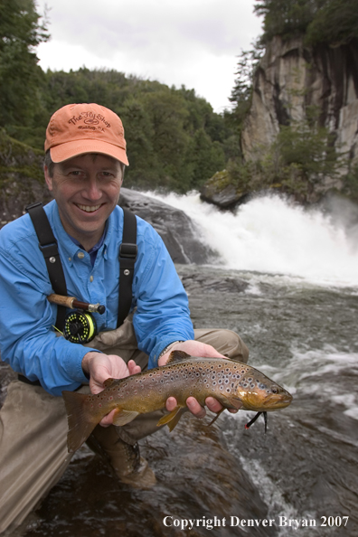 Flyfisherman holding brown trout.  Waterfall in background.