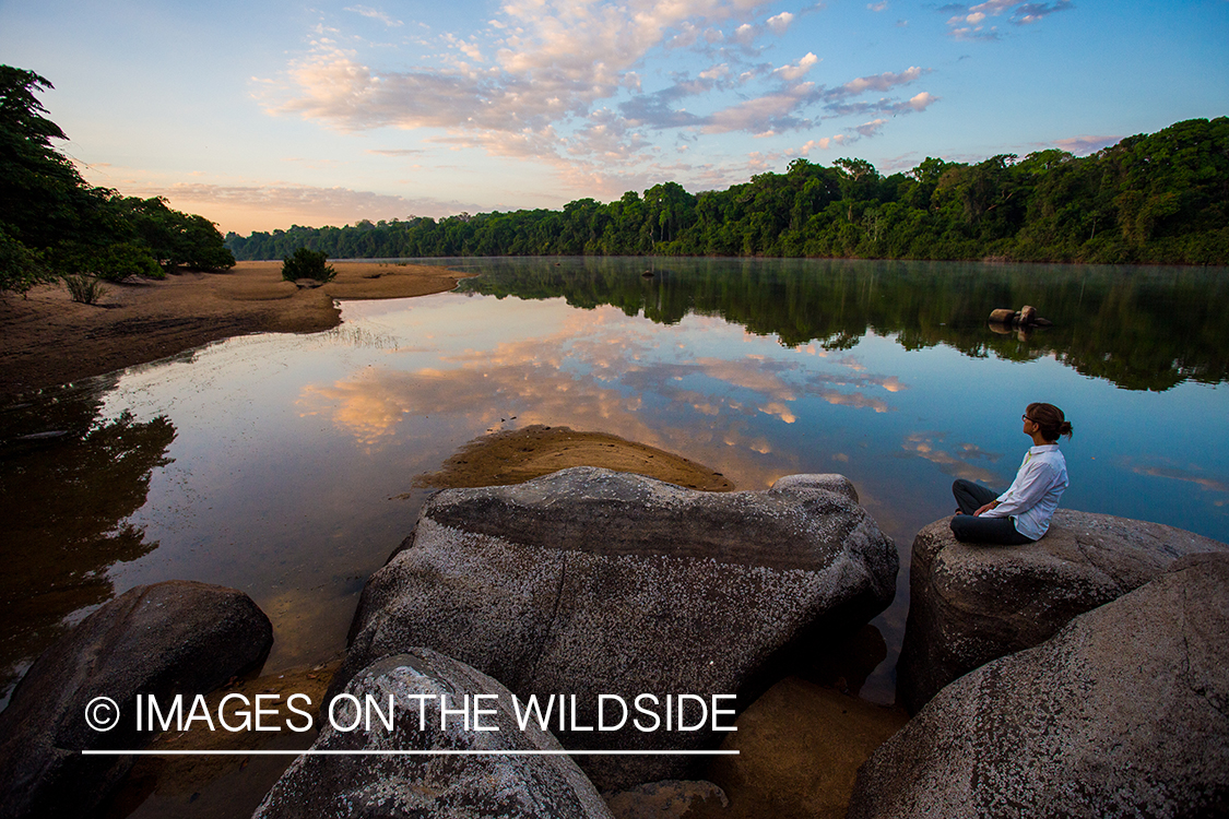 Woman sitting by river at sunset in Kendjam region, Brazil.