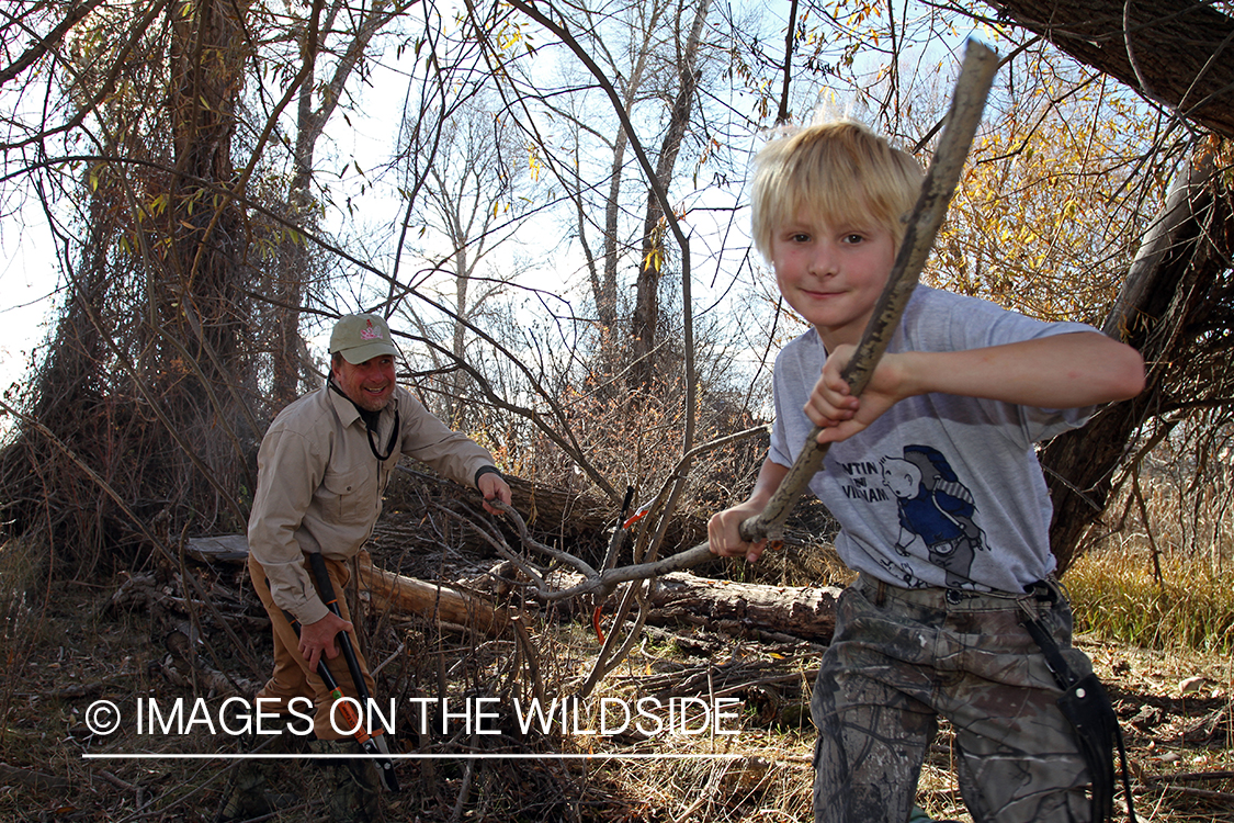 Father and son waterfowl hunters building blind.